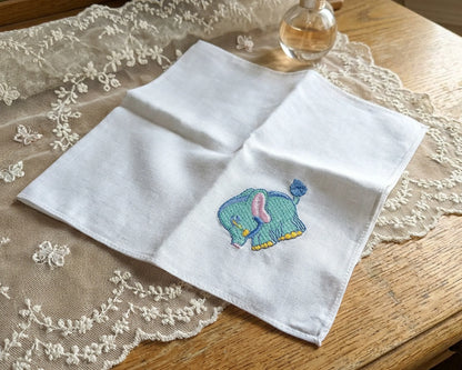 White handkerchief with a embroidered elephant design on a lace tablecloth.