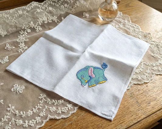 White handkerchief with a embroidered elephant design on a lace tablecloth.