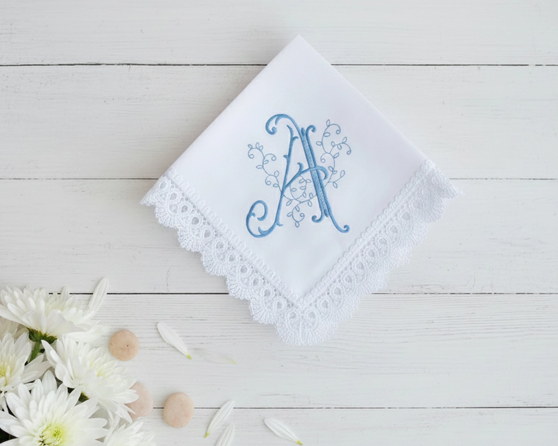 White handkerchief with blue embroidered letter 'A' on a wooden surface with flowers.