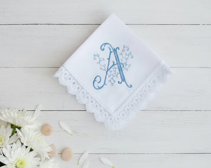 White handkerchief with blue embroidered letter 'A' on a wooden surface with flowers.