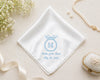 White handkerchief with blue embroidery on a beige surface with flowers and jewelry.