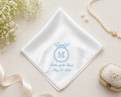 White handkerchief with blue embroidery on a beige surface with flowers and jewelry.
