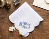 White handkerchief with blue monogram 'M.E.J.' on a wooden surface with decorative items.