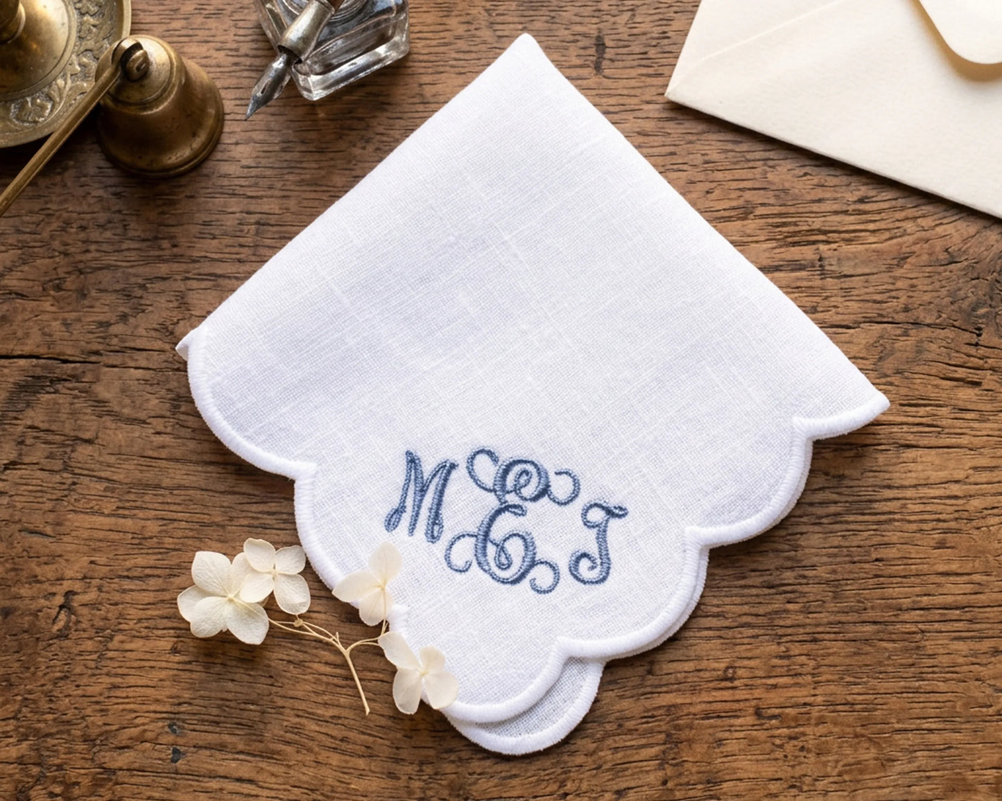 White handkerchief with blue monogram 'M.E.J.' on a wooden surface with decorative items.