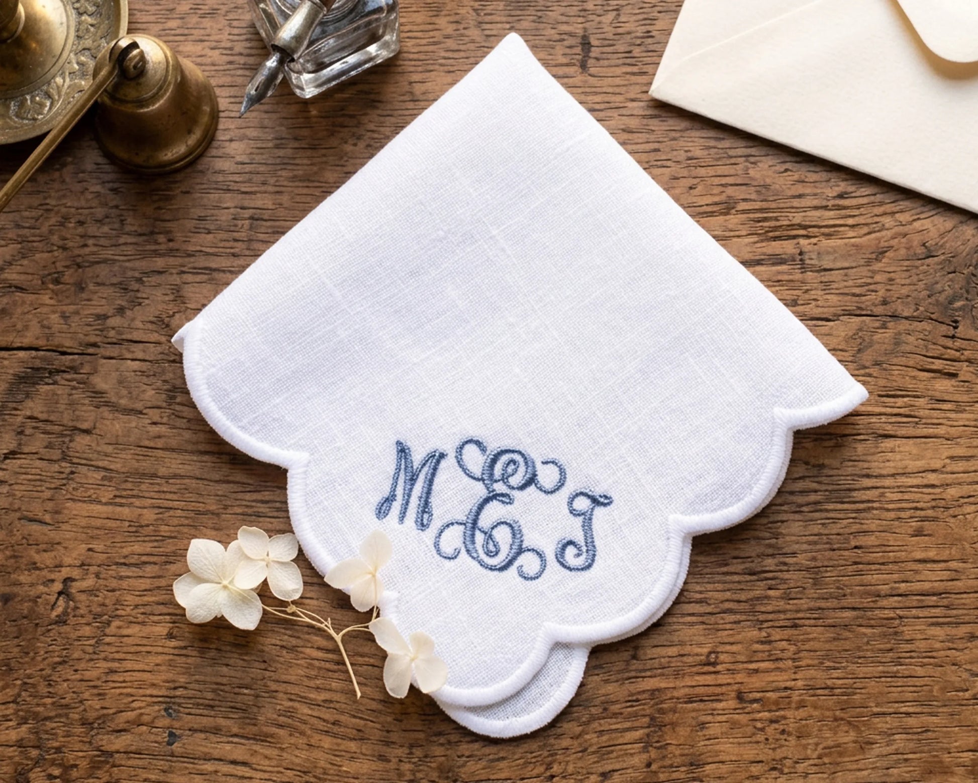 White handkerchief with blue monogram 'M.E.J.' on a wooden surface with decorative items.