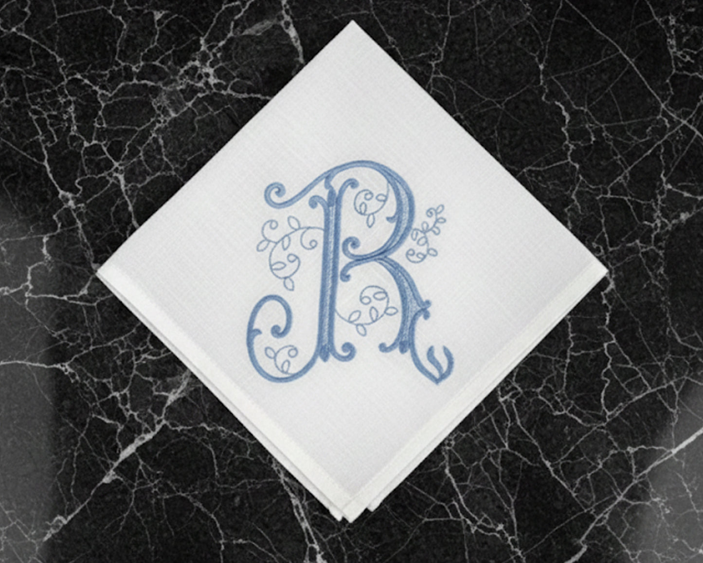 White handkerchief with blue monogram 'R' on a black marble surface