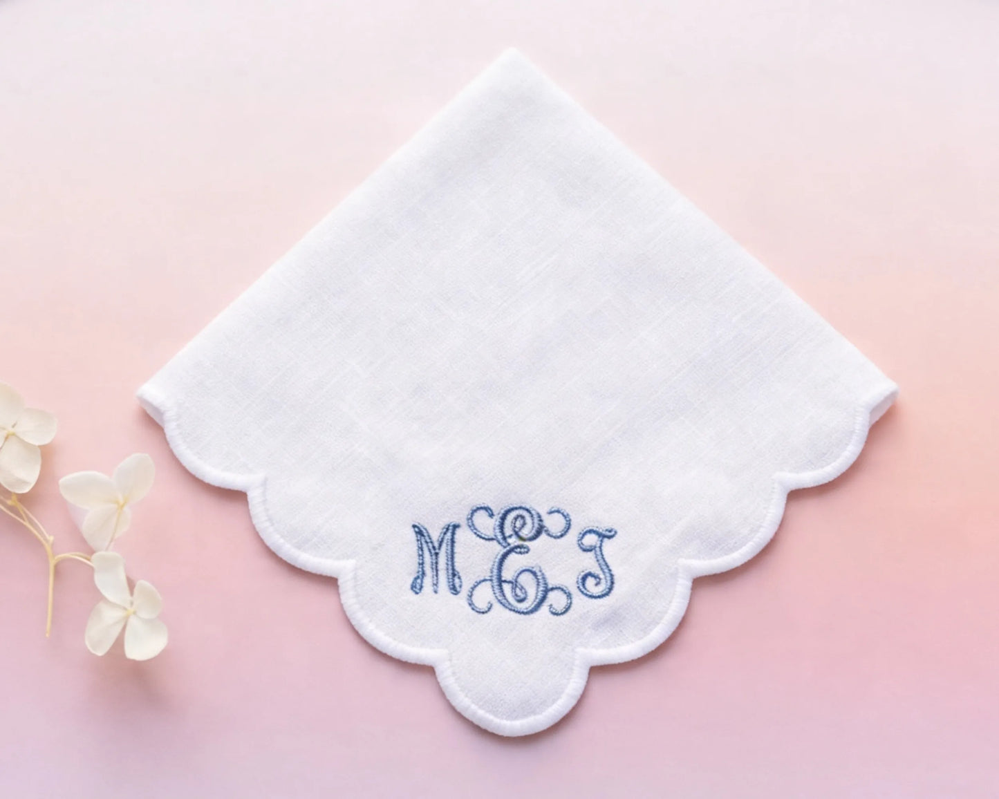 White handkerchief with embroidered initials 'MGS' on a pink background
