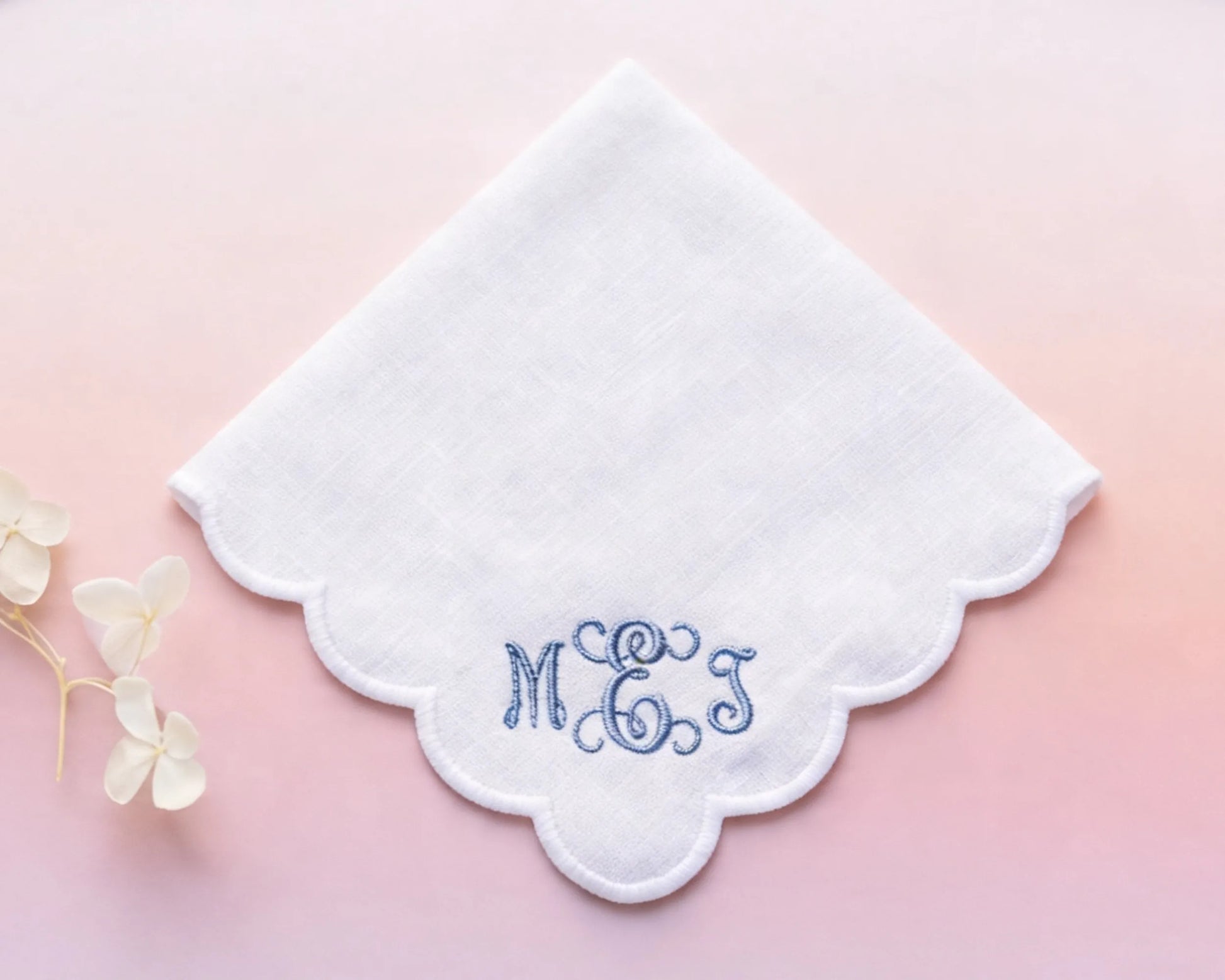 White handkerchief with embroidered initials 'MGS' on a pink background