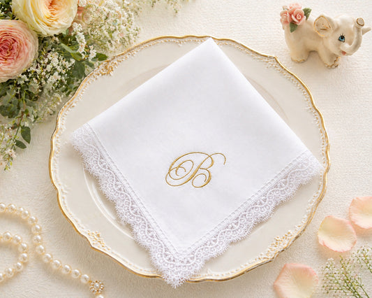 White handkerchief with gold monogram 'B' on a decorative plate with flowers and pearls.