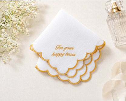 White handkerchief with gold text 'For your happy tears' on a light background with flowers and a perfume bottle.