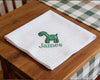 White handkerchief with green dinosaur design and 'James' text on a wooden table.