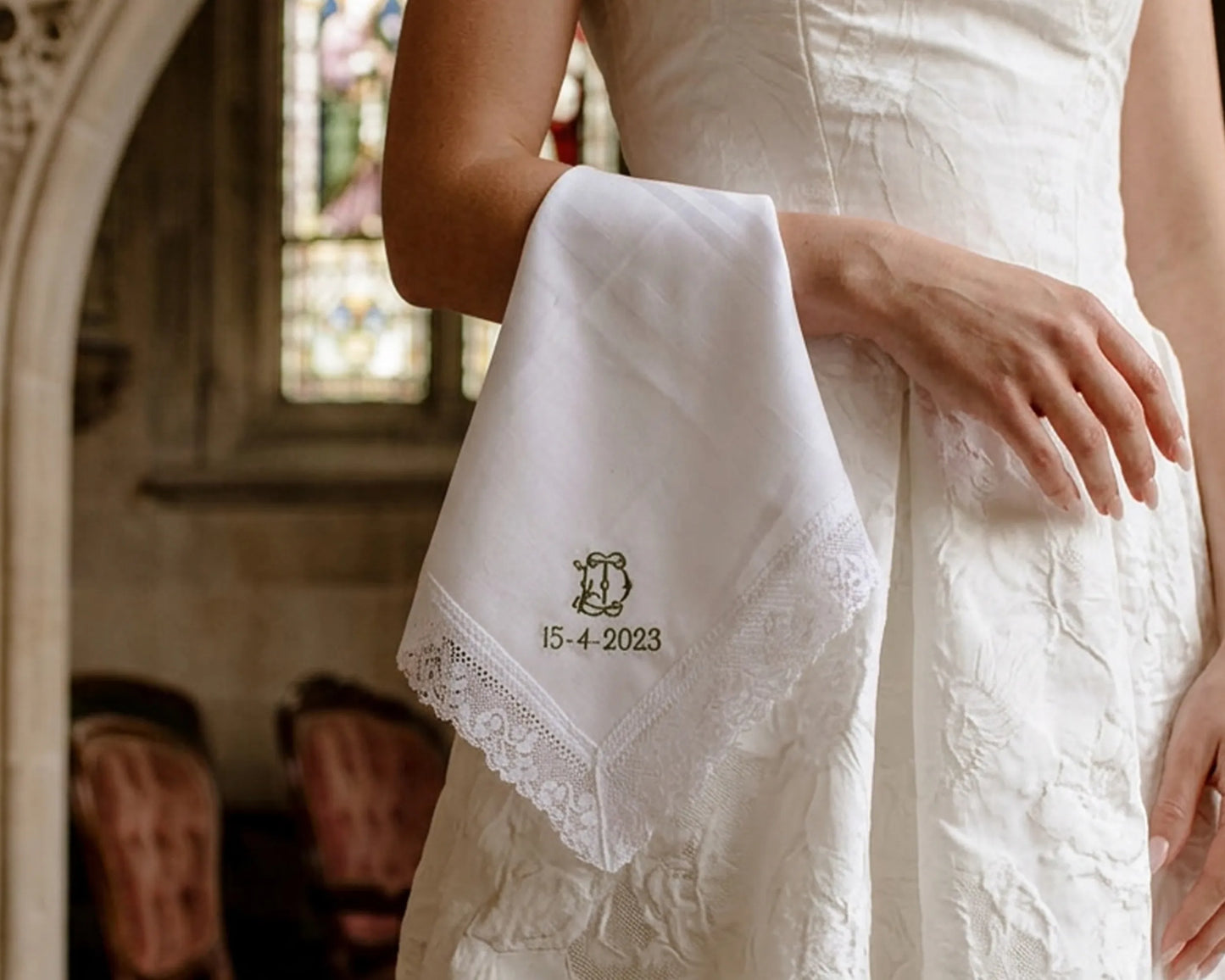 White handkerchief with lace details held by a person in a white dress, with '15-4-2023' printed on it, in an indoor setting.