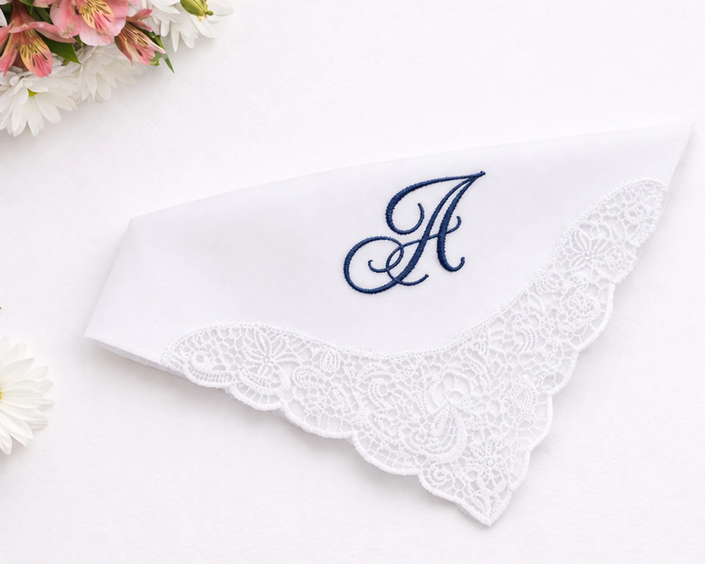 White handkerchief with lace edge and blue embroidered letter 'A' on a white background with flowers.