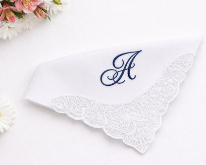 White handkerchief with lace edge and blue embroidered letter 'A' on a white background with flowers.