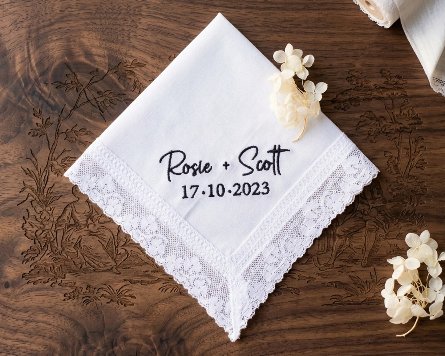 White handkerchief with personalized text on a wooden surface with floral decorations