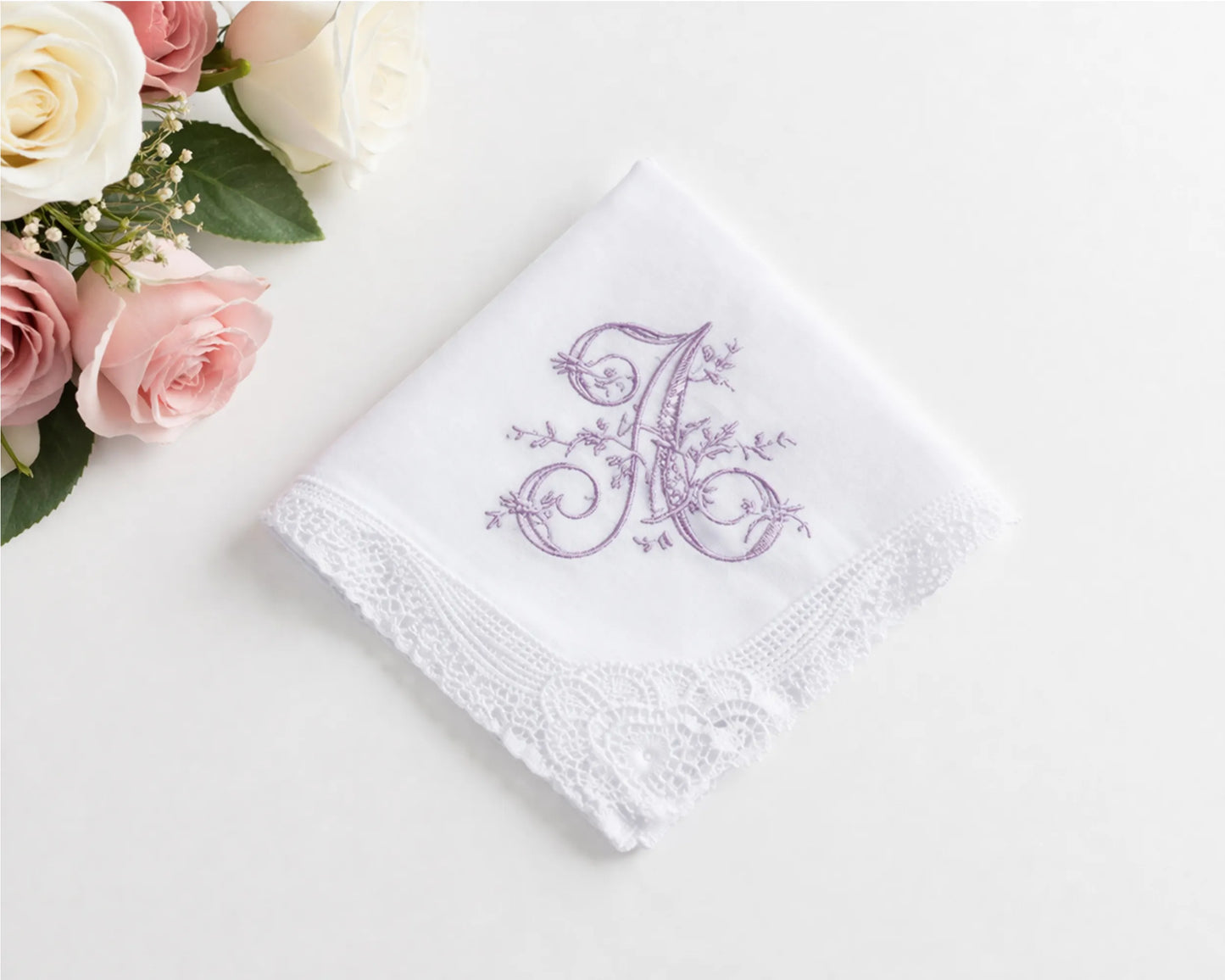 White handkerchief with purple floral monogram on a white surface with pink roses.