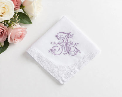 White handkerchief with purple floral monogram on a white surface with pink roses.