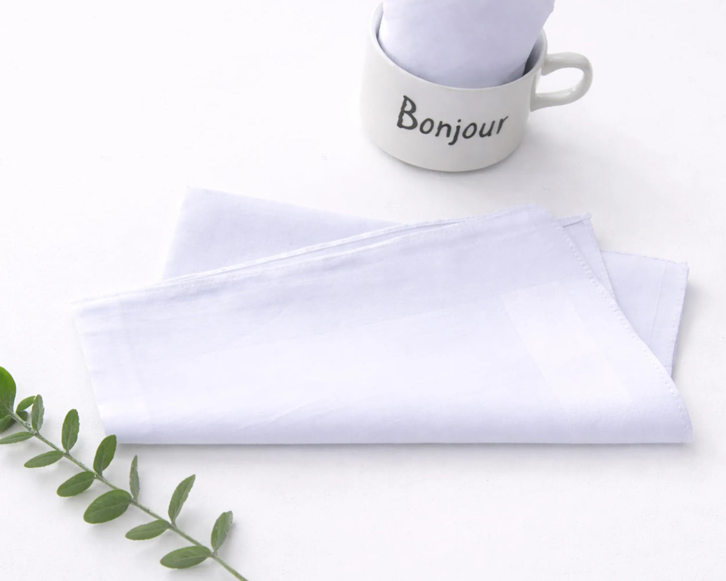 White hanky with 'Bonjour' text and folded white napkin on a light surface.