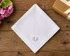 White hanky with 'JLB' monogram on a wooden surface with flowers and a gift box.