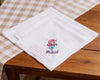 White hanky with embroidered mermaid design and 'Maud' text on a wooden table.