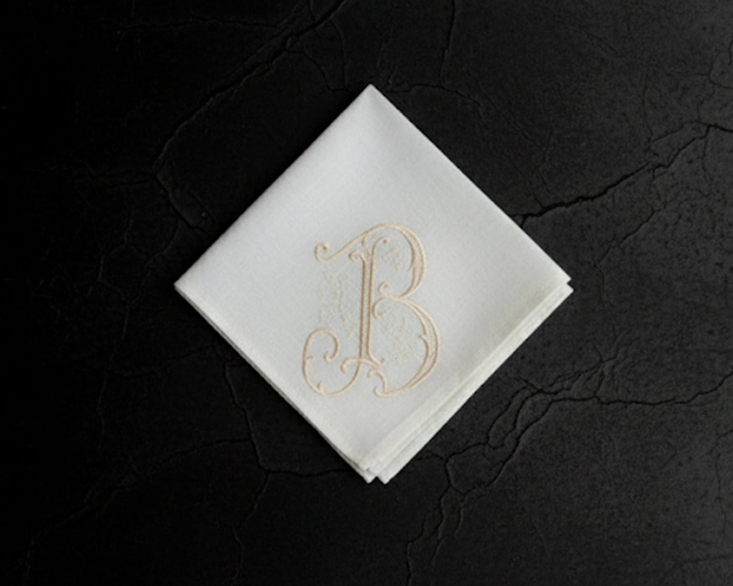 White hanky with gold letter 'B' on a dark textured surface