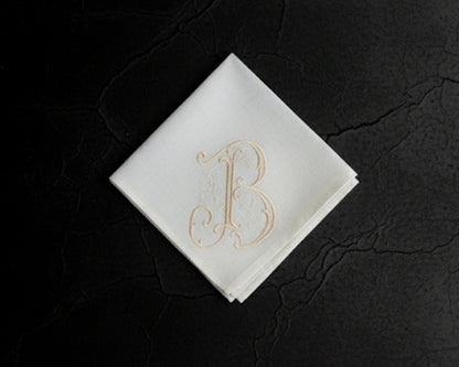 White hanky with gold letter 'B' on a dark textured surface
