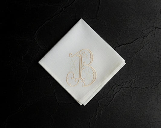 White hanky with gold letter 'B' on a dark textured surface