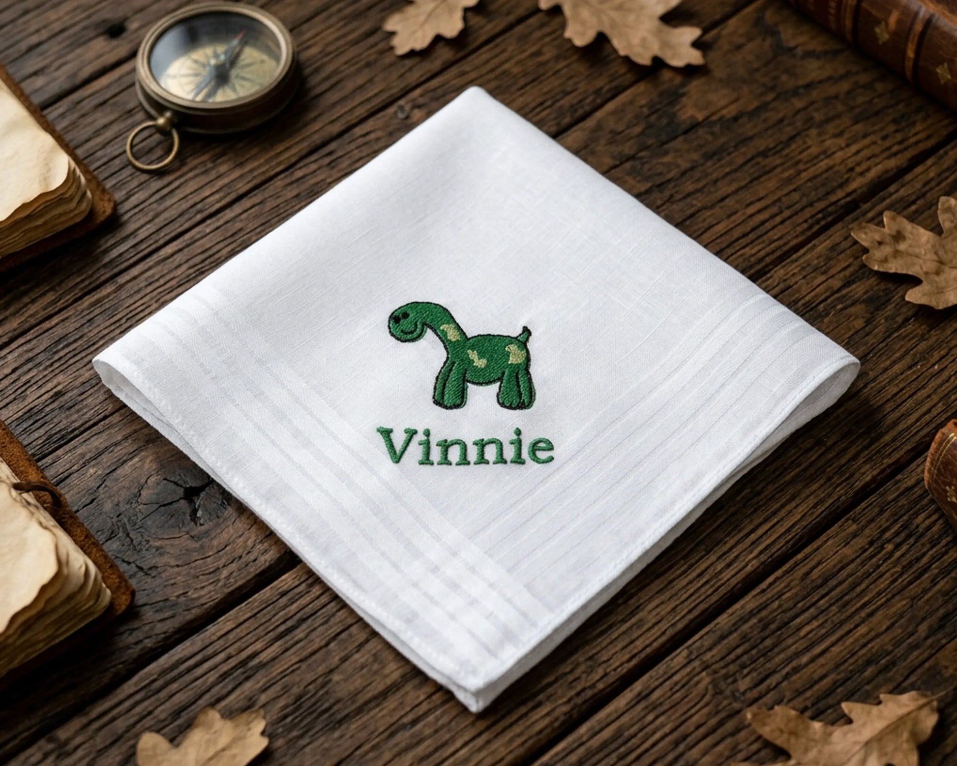 White hanky with green dinosaur design and 'Vinnie' text on a wooden surface