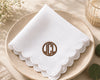 White hanky with lscalloped ace edge and embroidered monogram on a beige plate.