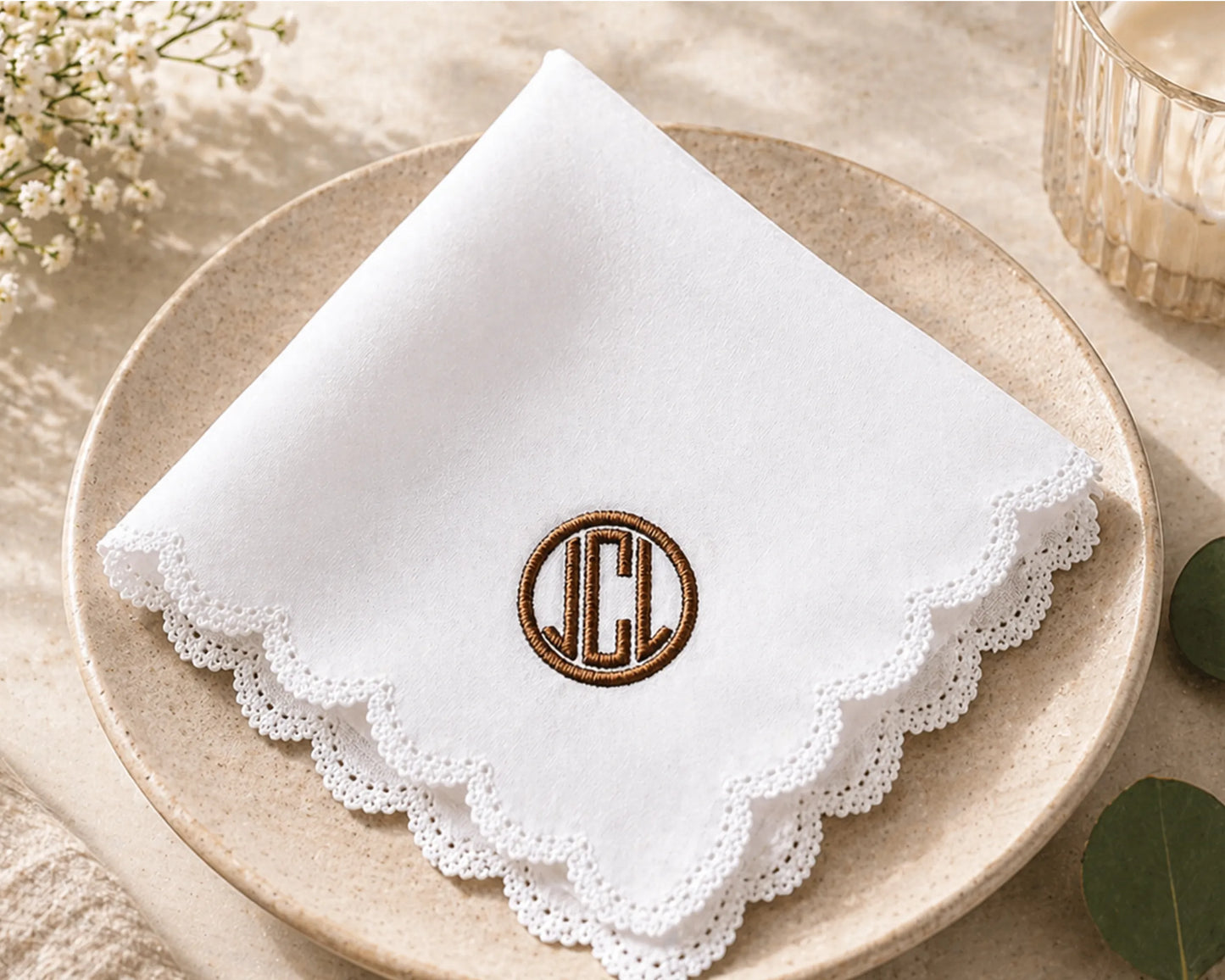 White hanky with lscalloped ace edge and embroidered monogram on a beige plate.