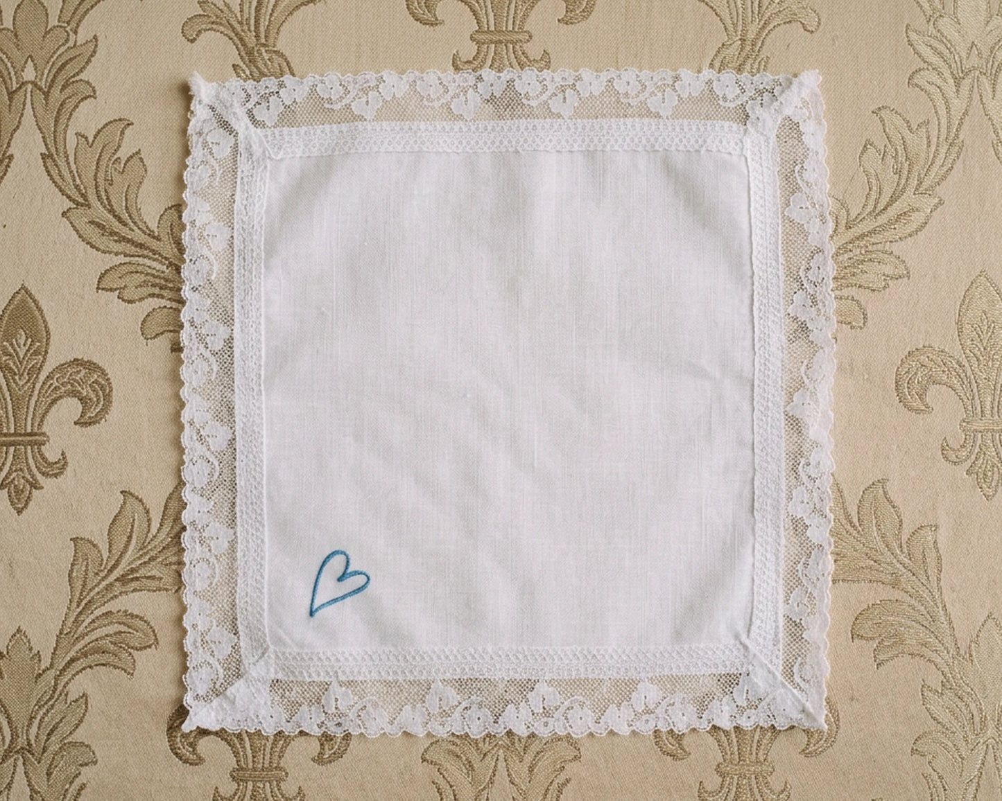 White lace-edged handkerchief with a blue heart on a patterned beige background