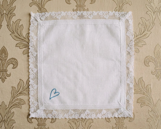White lace-edged handkerchief with a blue heart on a patterned beige background