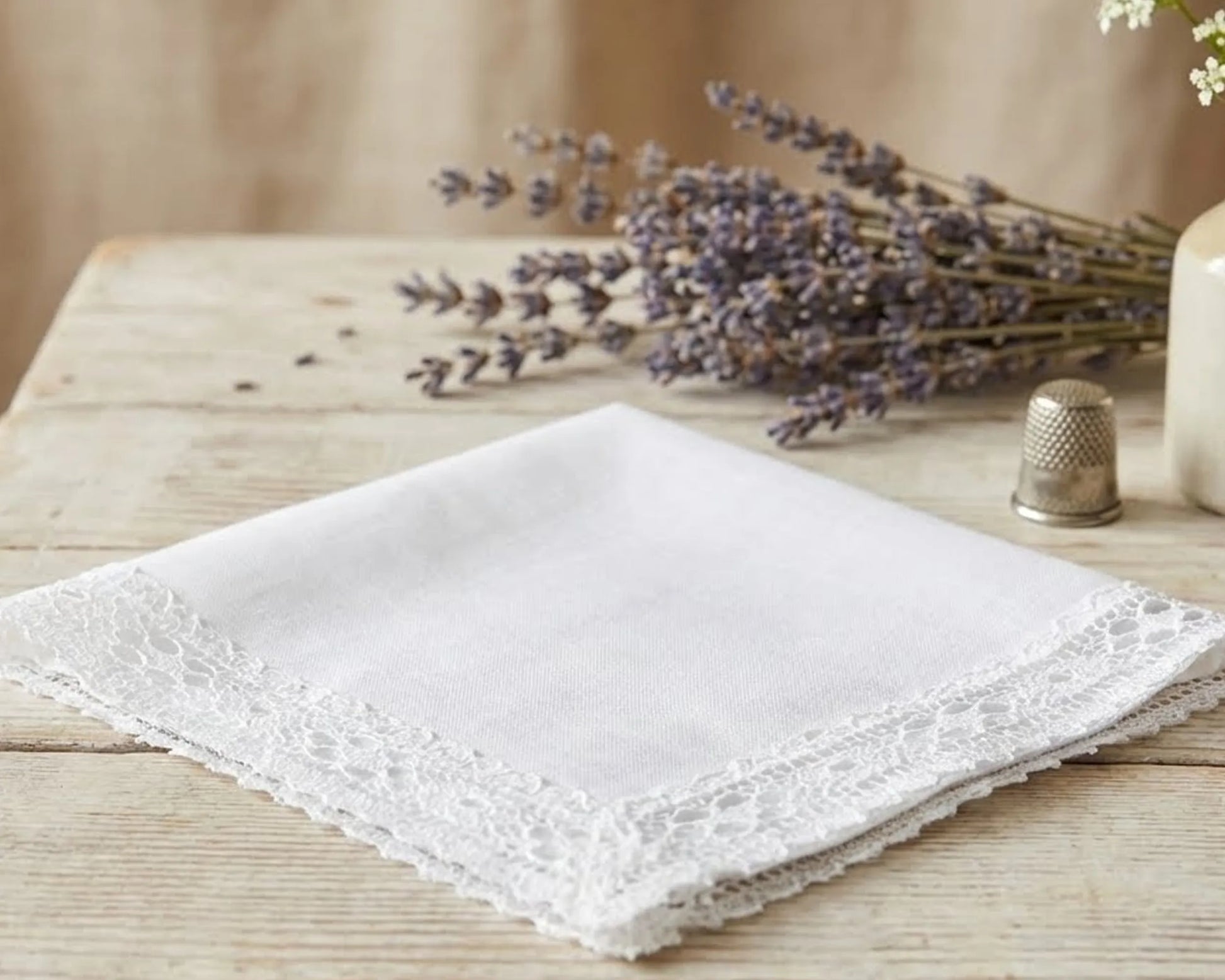 White lace-handkerchief on a wooden surface with lavender and a thimble.