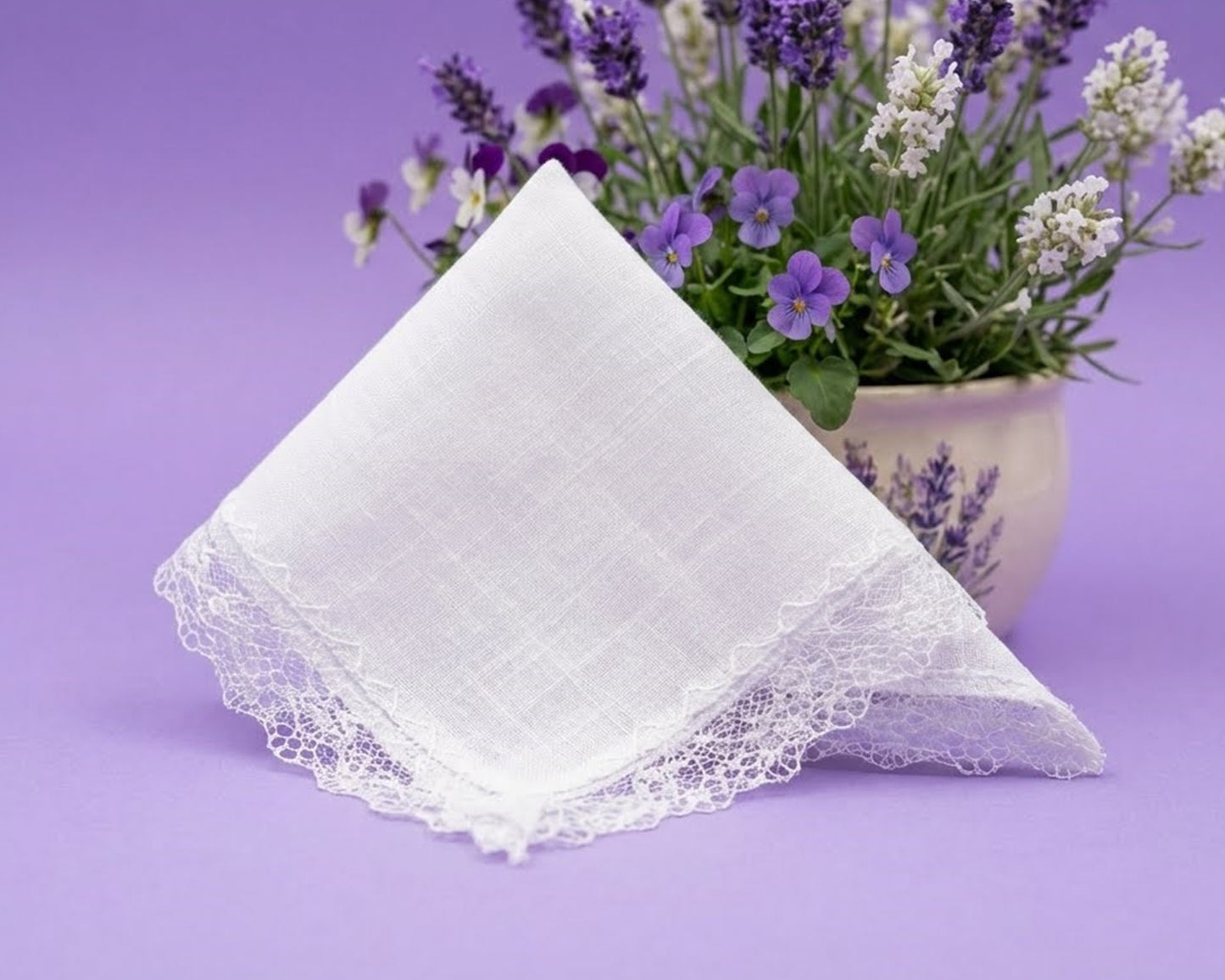 White lace-trimmed handkerchief on a purple background with a potted plant.