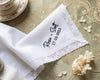 White lace-trimmed handkerchief with embroidered text on a decorative tablecloth.