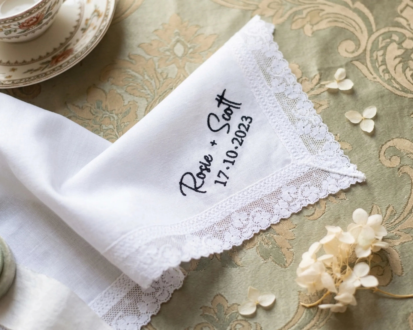 White lace-trimmed handkerchief with embroidered text on a decorative tablecloth.