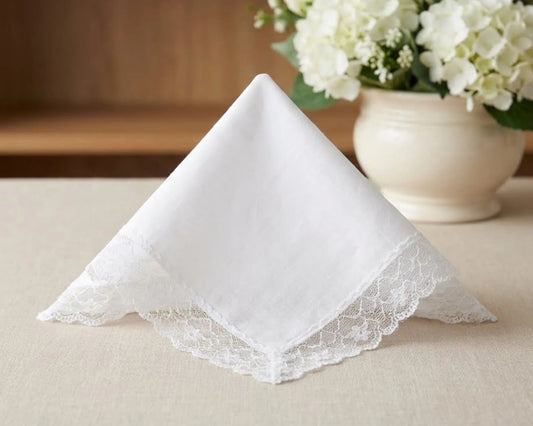 White lace-trimmed handkerchief on a beige surface with a vase of white flowers in the background.