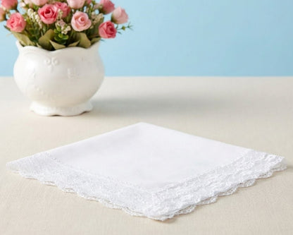 White lace handkerchief on a beige surface with a vase of pink flowers in the background.