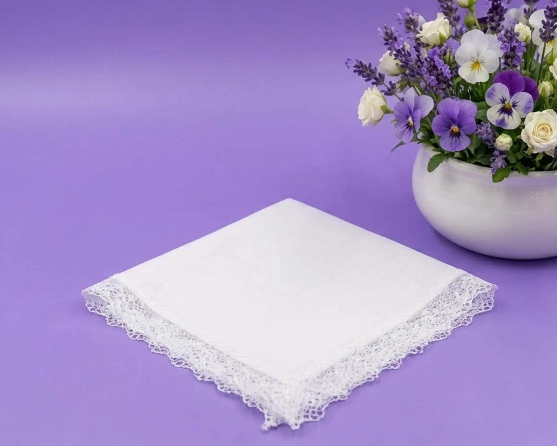 White lace handkerchief on a purple background with a vase of flowers.