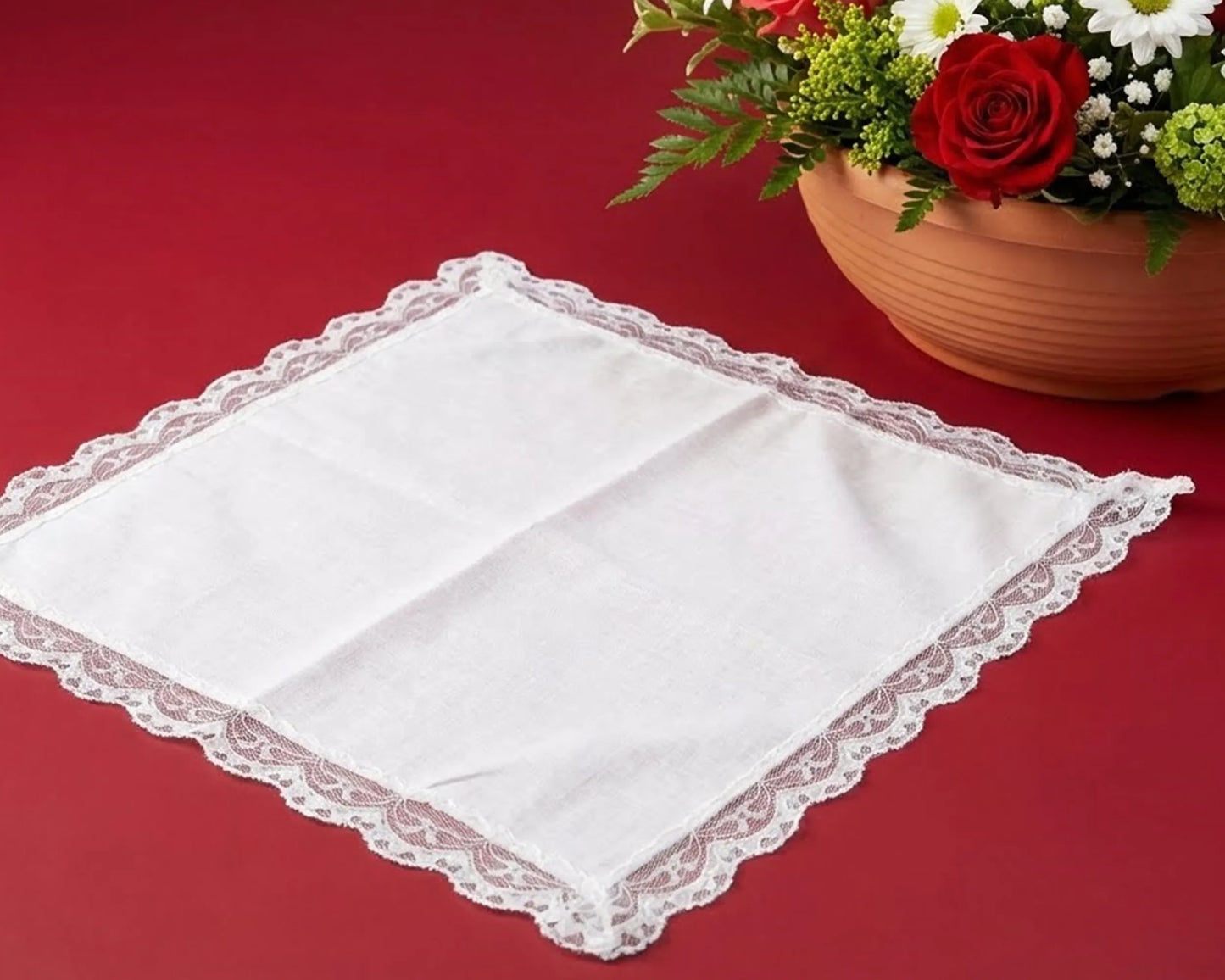 White lace doily on a red surface with a vase of flowers.