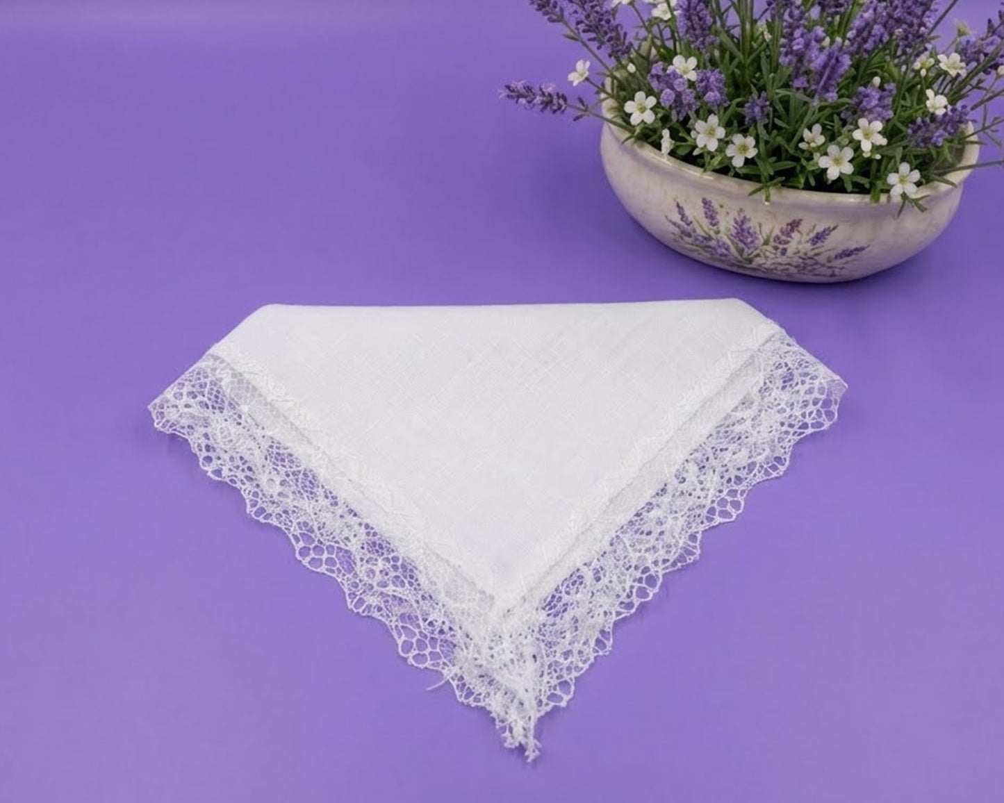 White lace handkerchief on a purple background with a bowl of flowers.