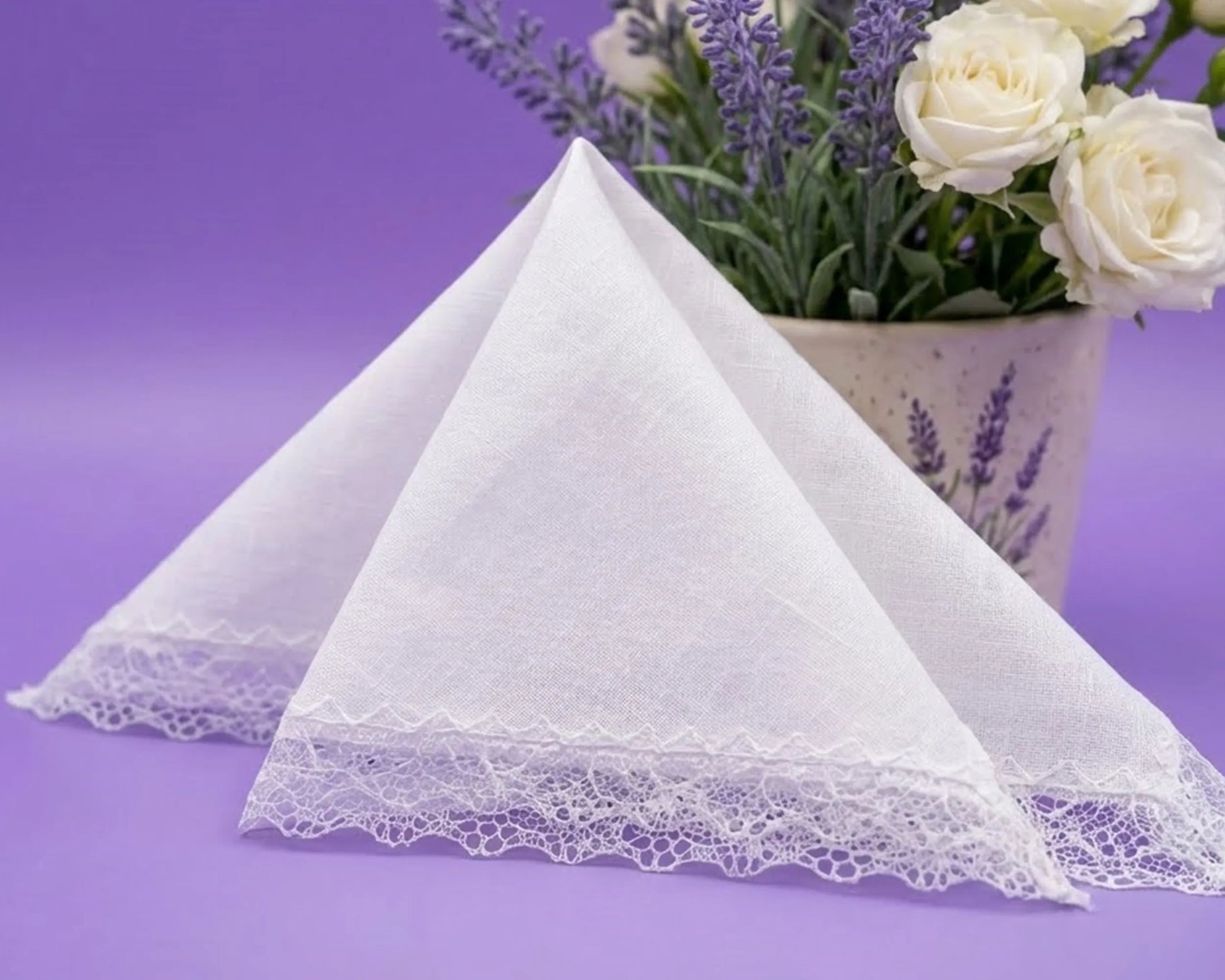 White lace-trimmed handkerchief on a purple background with a vase of flowers.