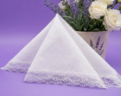 White lace-trimmed handkerchief on a purple background with a vase of flowers.