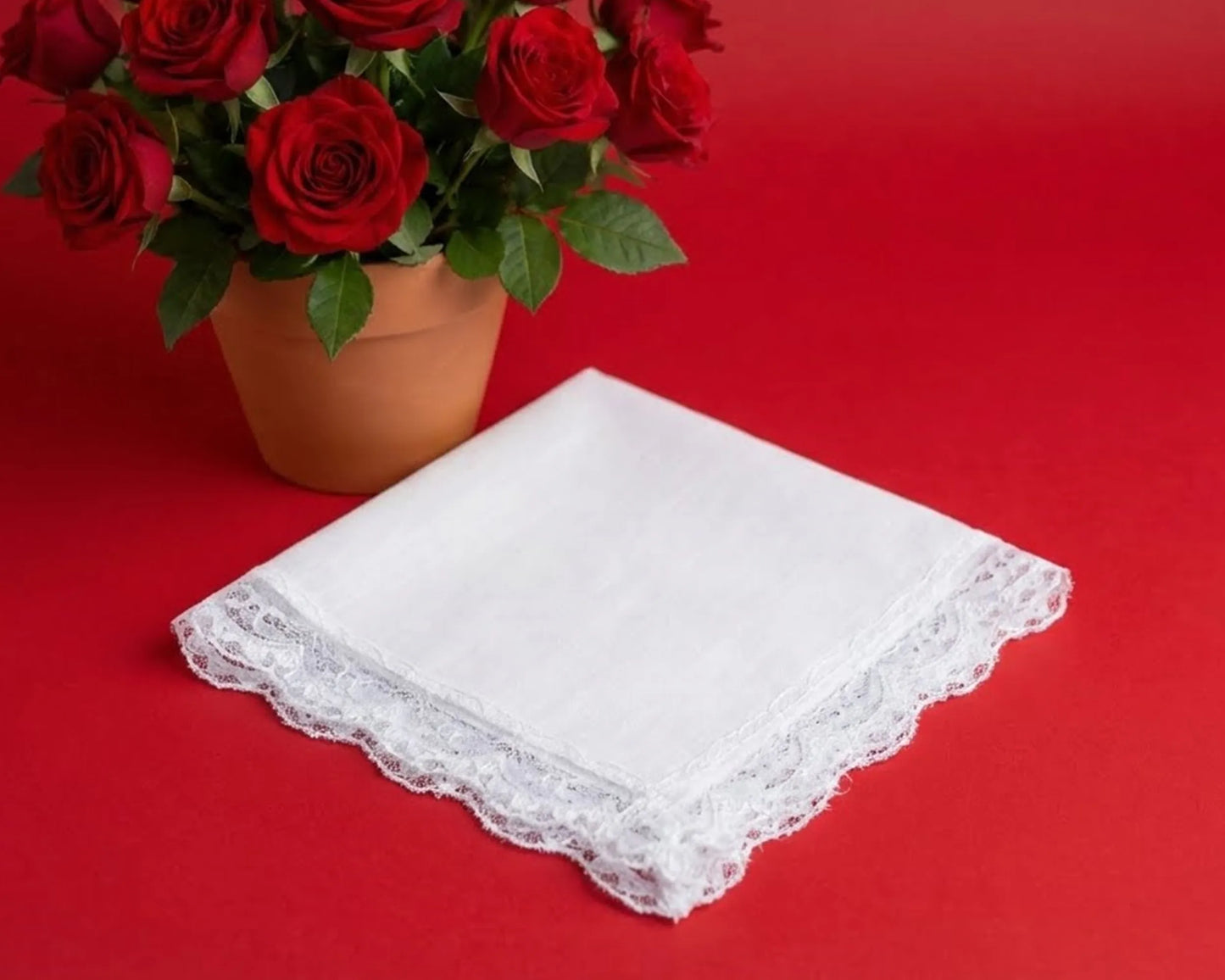 White lace handkerchief on a red background with a potted plant of red roses.