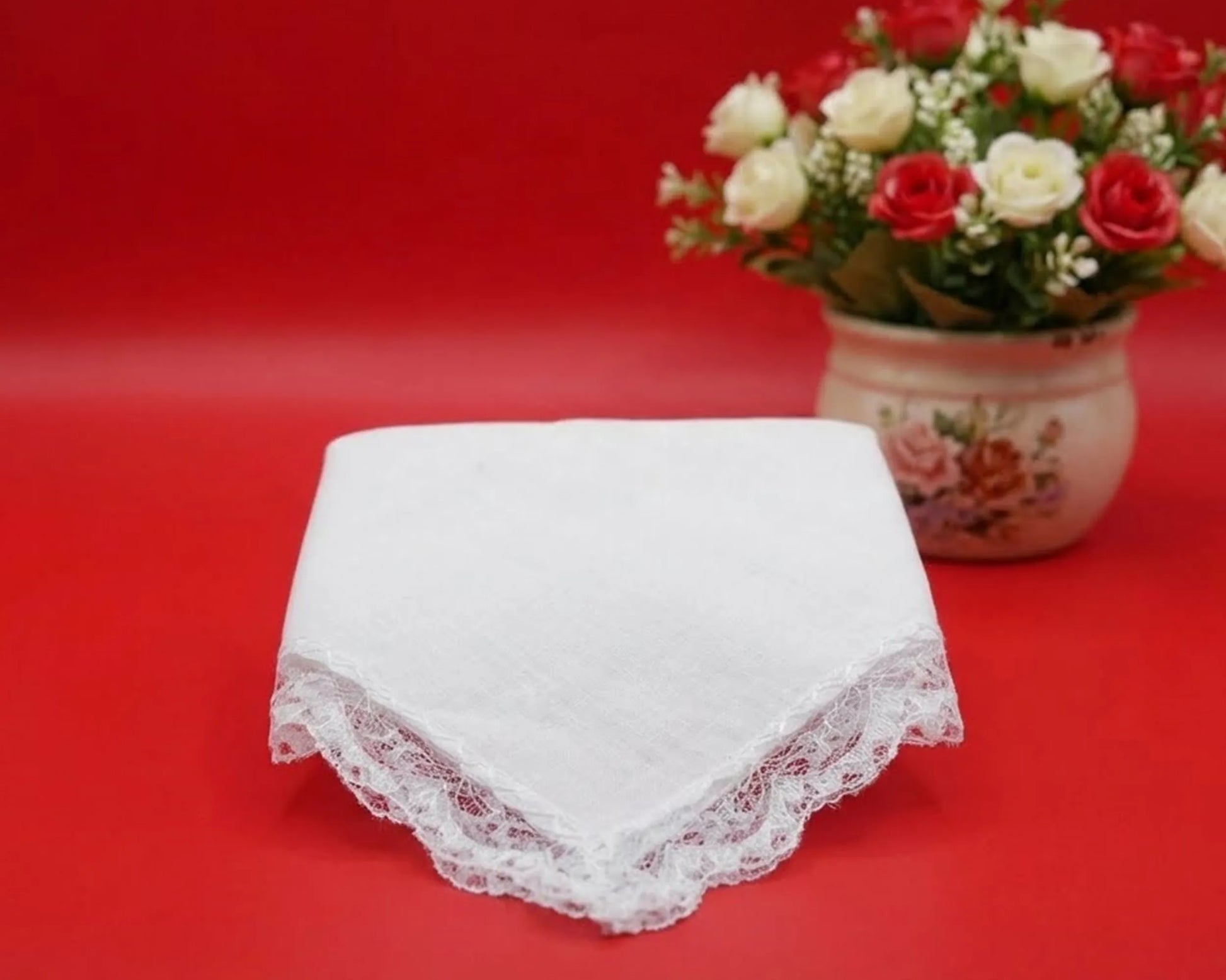 White lace handkerchief on a red background with a floral arrangement.