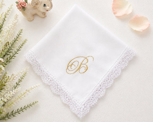 White lace handkerchief with gold letter 'B' on a light surface with decorative elements.