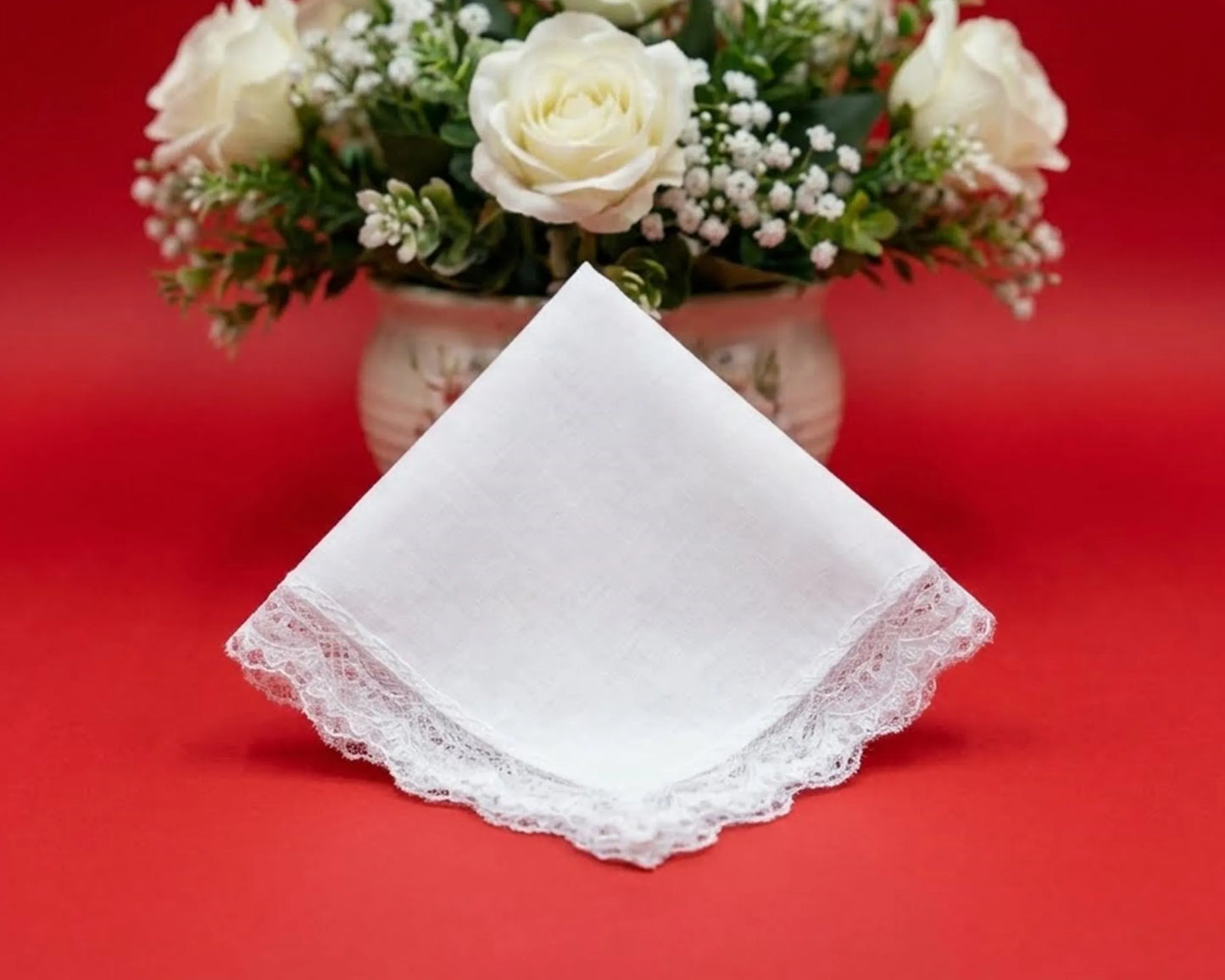 White lace handkerchief on a red background with a vase of white flowers.