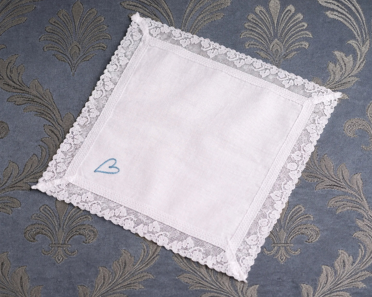 White lace hanky with a blue heart on a patterned fabric background