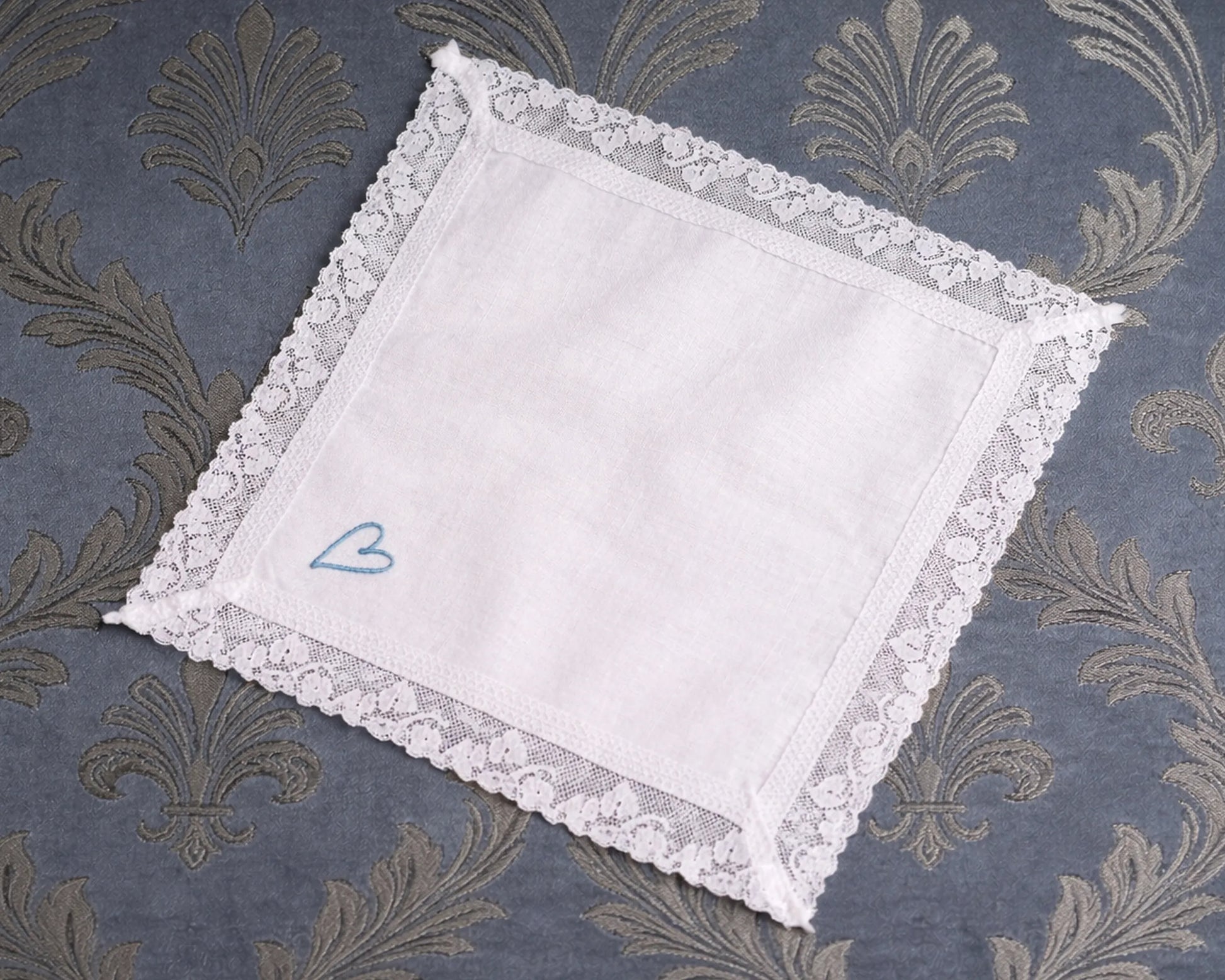 White lace hanky with a blue heart on a patterned fabric background