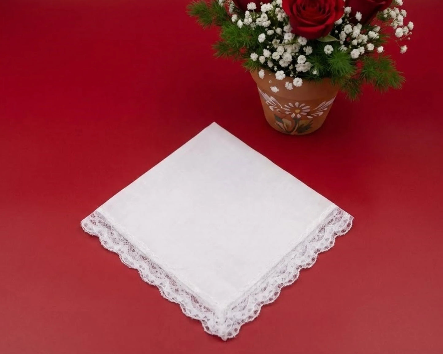 White lace handkerchief on a red surface with a potted plant in the background